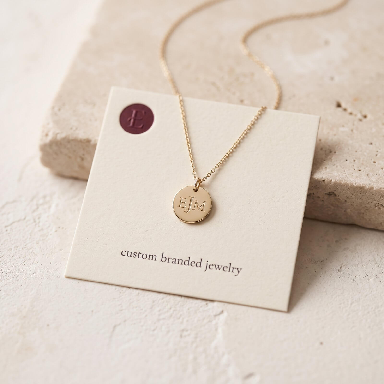 A logo-engraved jewelry piece on a custom branded card, shot calm and editorial on a stone surface.