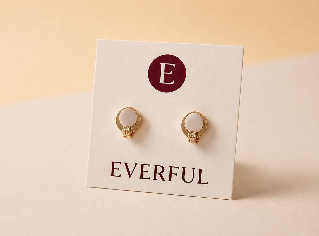 Earrings presented on a custom branded card carrying the retailer's name, on a stone surface.