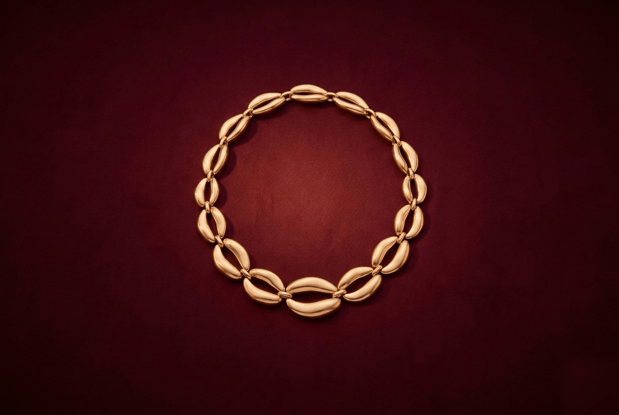 A single gold-tone statement necklace on a deep burgundy background, lit warmly with soft shadow.