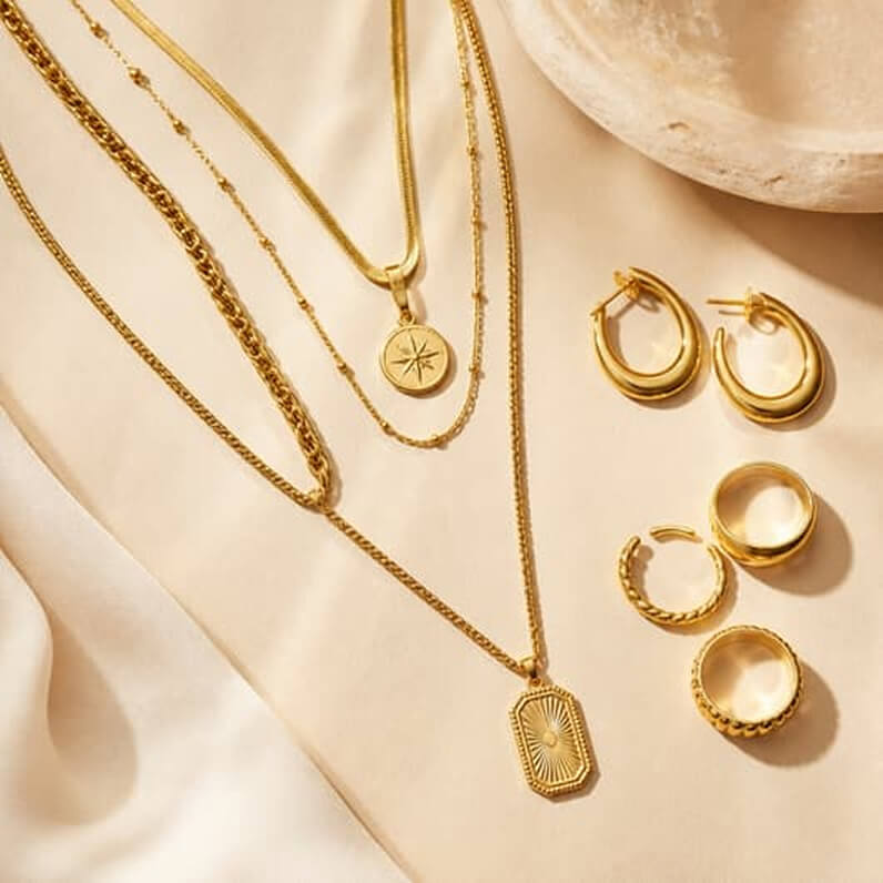 Layered gold chains, hoops and rings on a stone surface