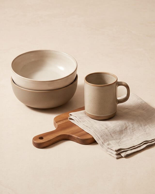 Stacked ceramic bowls, a mug, a wooden board and a linen towel on a stone surface