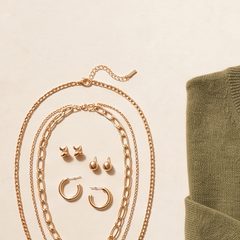 Layered gold chains and hoop earrings on a stone surface