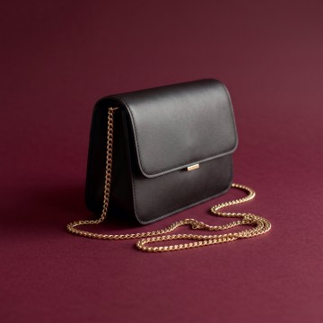 A black chain-strap handbag on a plum background