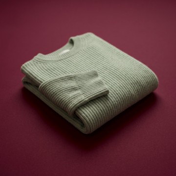 A folded sage knit sweater on a plum background