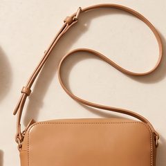A tan leather crossbody bag on a stone surface