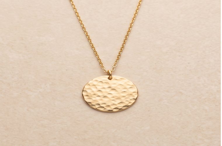 A plain hammered gold pendant necklace on a stone surface
