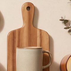 A ceramic mug and a wooden serving board on a stone surface