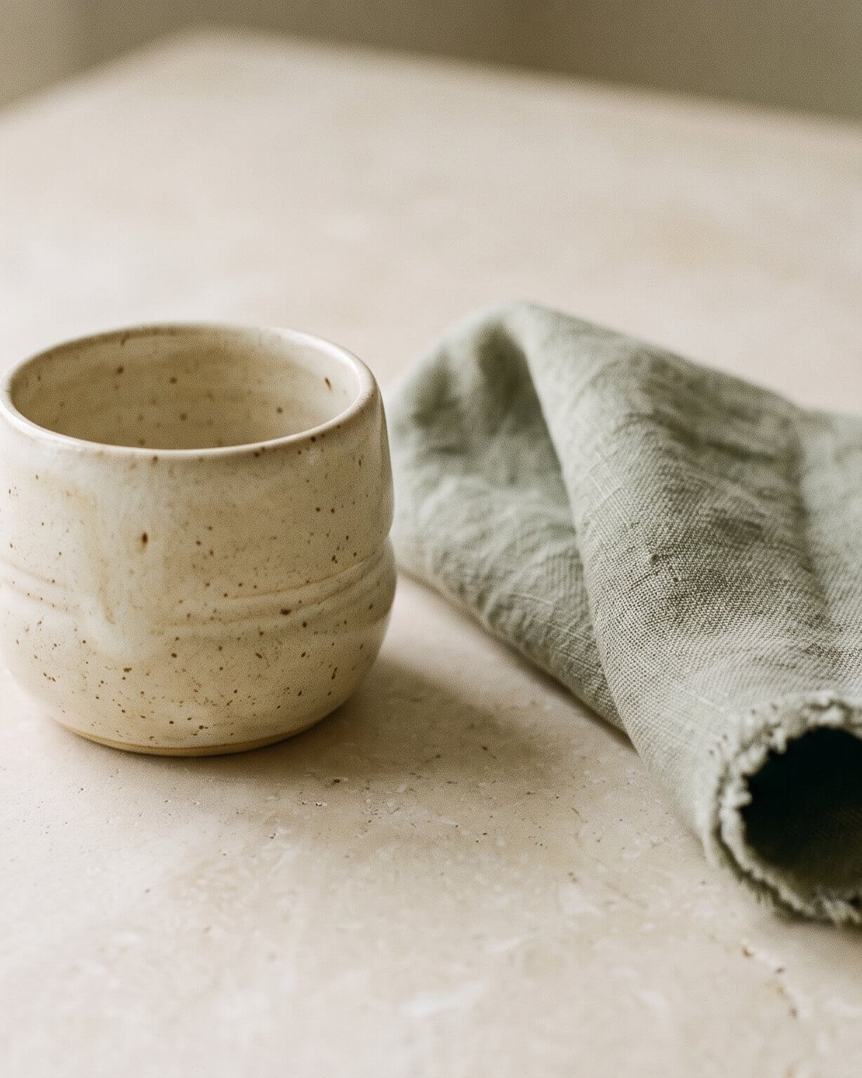 A custom ceramic vessel and folded sage linen on a stone surface, a home and lifestyle piece made to order.