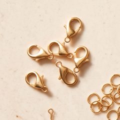 Gold lobster clasps and jump rings on a stone surface