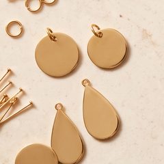 Blank gold pendant discs and teardrops on a stone surface