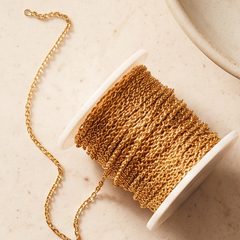 A spool of fine gold chain on a stone surface
