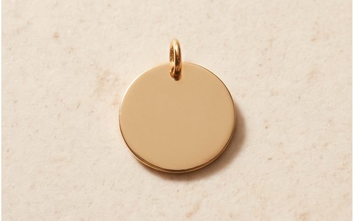 A single blank gold pendant disc on a stone surface