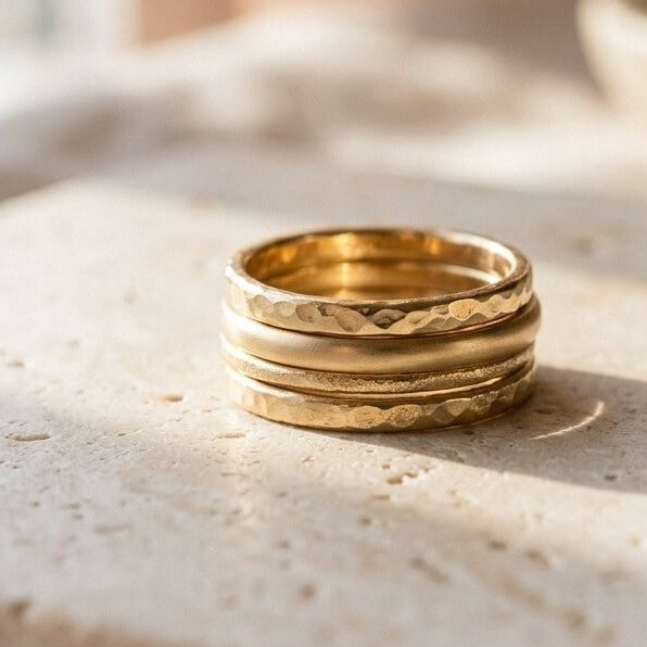 Stack of hammered gold-tone rings on a warm stone surface
