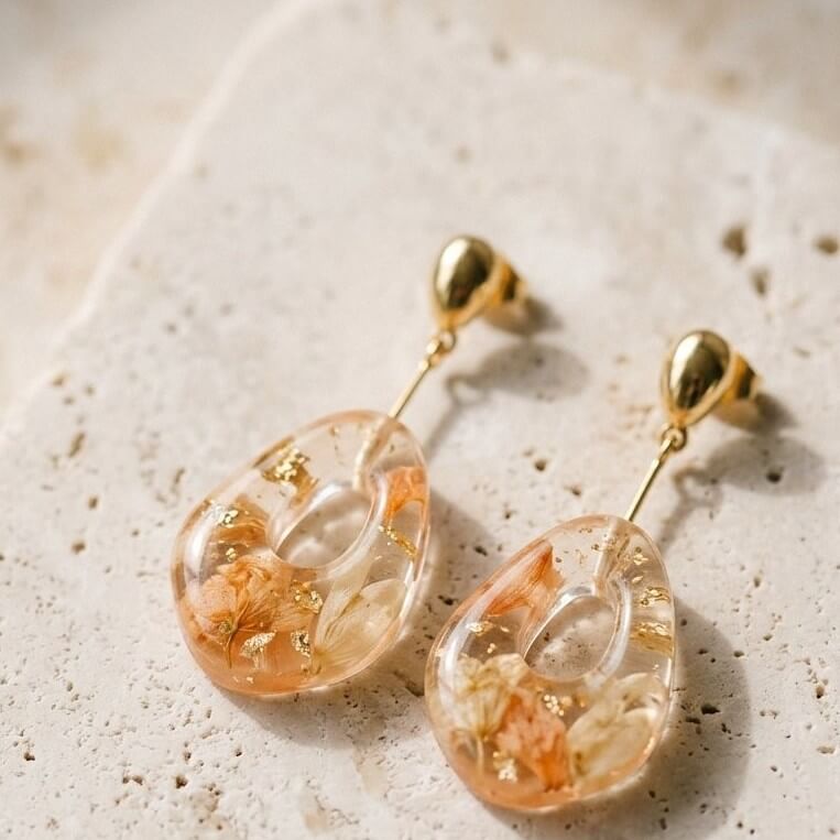 Pair of resin drop earrings with pressed flowers on a warm stone surface
