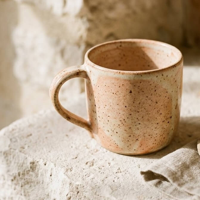 Speckled ceramic mug with dried botanicals on a warm stone ledge