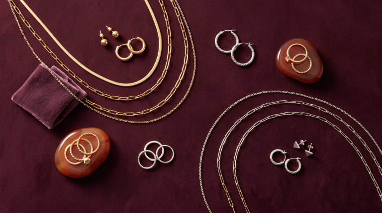 Gold and silver jewelry arranged on a deep burgundy surface with carnelian accents, overhead editorial still life.
