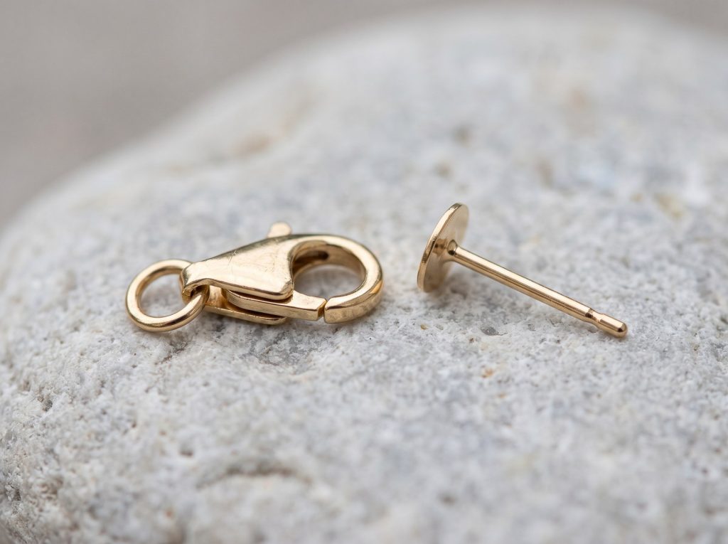A lobster clasp and an earring post in close detail, the contact points where jewelry most often fails