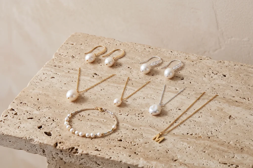 Pearl bridesmaid jewelry on travertine: gold and silver pearl drop earrings, three pearl pendant necklaces, a pearl bracelet and a gold initial pendant