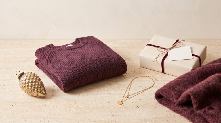 A curated Christmas assortment of an ornament, folded knit, jewelry, a wrapped gift, and a throw on a stone surface