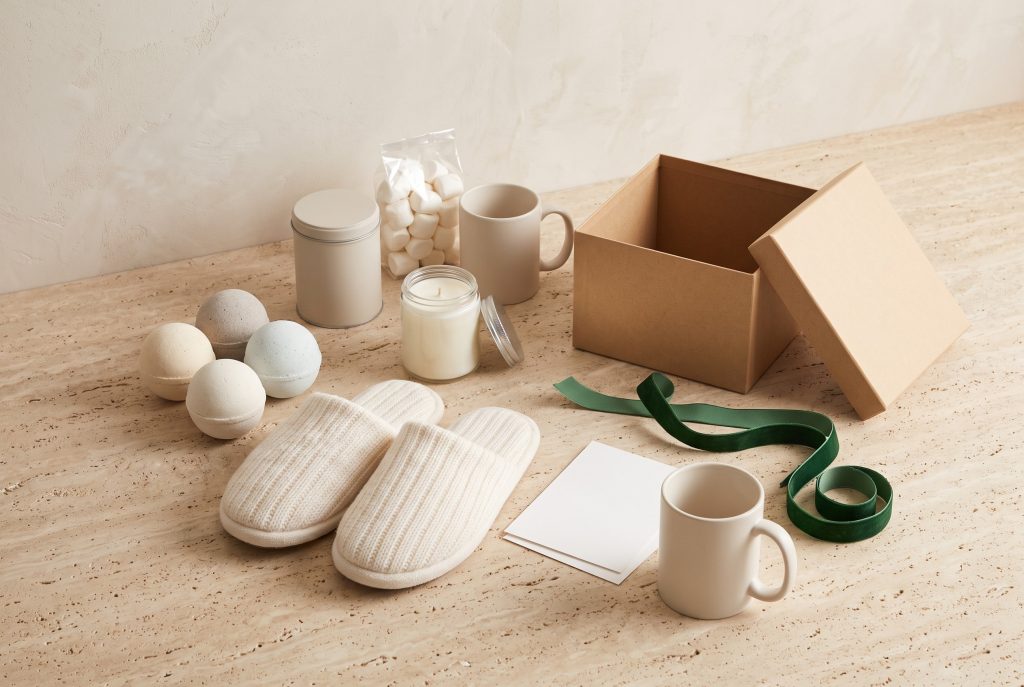 Bath bombs, slippers, a candle, and a hot chocolate kit with a gift box and ribbon on a stone surface