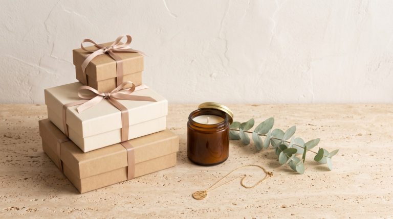 A curated holiday gift spread of wrapped gifts, jewelry, and a candle on a stone surface
