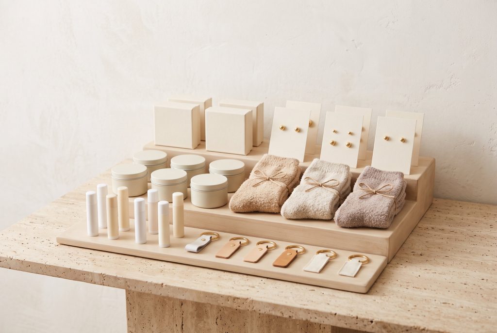 A tiered wooden display of lip balms and keychains, candle tins and folded socks, with jewelry boxes and gold stud earrings behind