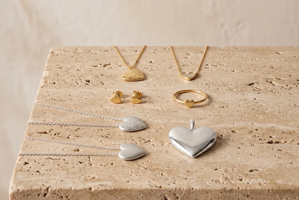 Heart jewelry on travertine: hammered and pave gold pendant necklaces, gold heart studs and a heart ring, and three silver heart pendants in different finishes