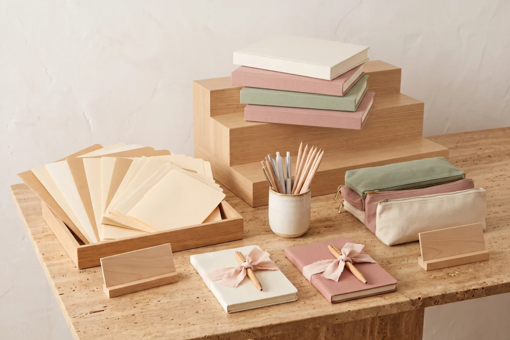 A retail display of blank journals on a wooden riser, fanned folders, stacked pencil cases and two ribbon-tied gift bundles