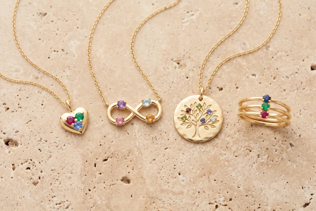 A gold heart pendant with three stones, an infinity pendant with four stones, a tree of life disc set with colored stones, and a stacked three-stone ring