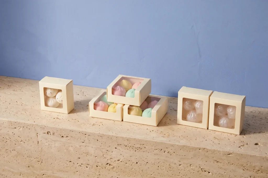 Boxed dumpling squishies in three styles, one box of classic white, three boxes of pastel and two of glitter, against a cornflower blue wall